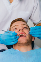 Fototapeta premium Smiling young man sitting in dentist chair while doctor examining his teeth.