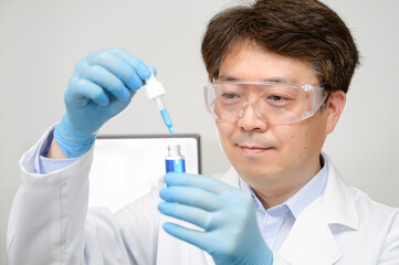 Portrait of a middle-year Asian male scientist wearing a white lab gown and gloves and holding an experimental container in his hand.