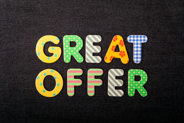 Card with Great Offer words made from mixed vivid colored wooden letters on a textured dark black textile material that can be used as a message.