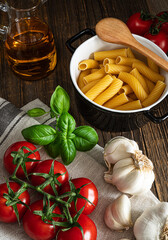 Pasta, garlic, basil, tomatoes and olive oil on the dark wooden table in the rustic kitchen.Ingredients for cooking Italian pasta..