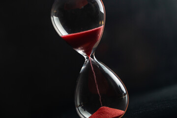 Sand passes through an hourglass, measuring the travel time counting down to the deadline, against...