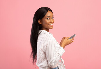 Young African American woman with smartphone talking to family or friends, having business meeting on pink background