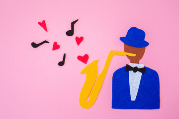International Jazz Day. A silhouette of a musician with a saxophone from which hearts and melodies flew out, on a pink background, cutted out of felt. Flat lay