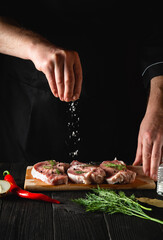 The chef sprinkles the meat with salt. Preparing meat before baking. Working environment in the kitchen of restaurant or cafe