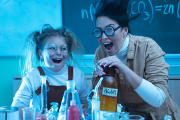 Teacher and little girl during chemistry lesson mixing chemicals in a laboratory