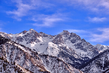 Majestic rocky peaks with fir forest against a blue sky with clouds  in the winter season