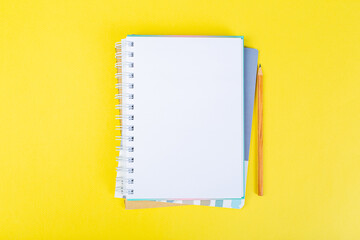open notepad on yellow background with pencil on top, spiral notepad with blank sheet.