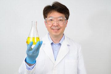 Portrait of a middle-year Asian male scientist wearing a white lab gown and gloves and holding an...