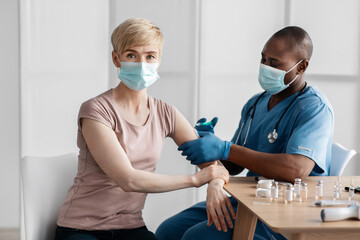 Adult african american lady sitting at doctor's office and getting modern Covid 19 shot injection...