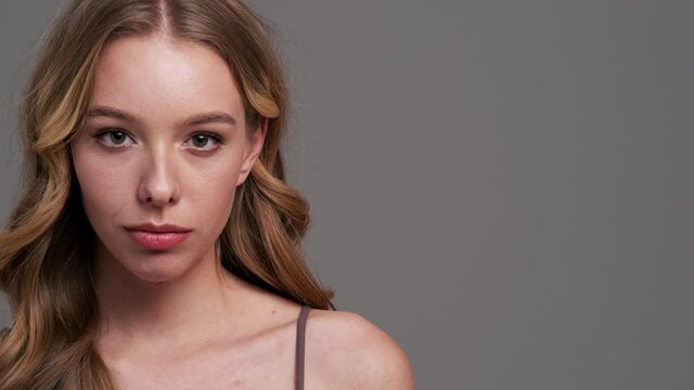 An attractive young woman is showing secret gesture standing isolated over gray background in studio
