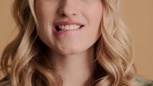 A close-up cropped view of a sexy young woman is biting her lip standing isolated over beige background in studio