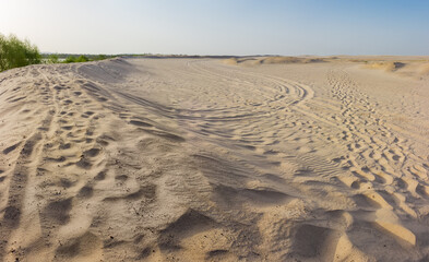 Sandy plain with dunes, footprints and tracks against clear sky