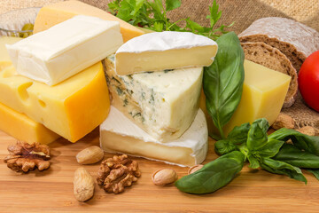 Different types cheese among greens and nuts on wooden surface