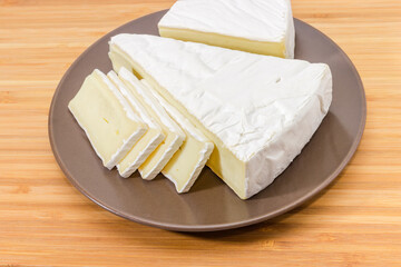 Pieces of brie cheese on brown dish on wooden surface