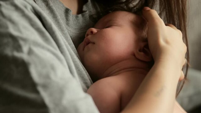 Mother holds new born baby in her arms, strokes his hair while he sleeps, lulls him to sleep with tenderness and care for the child. Maternity and motherhood concept.