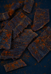 Beef jerky with hot pepper on black stone surface. Dried meat.