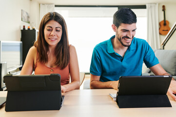portrait of smiling young couple working at home with two tablets