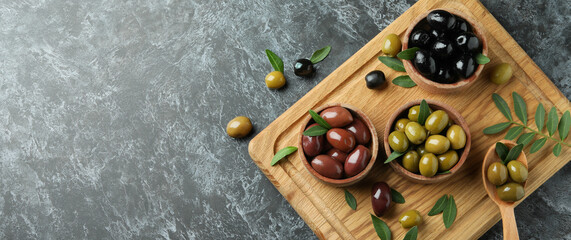 Board with olives and leaves on black smokey background