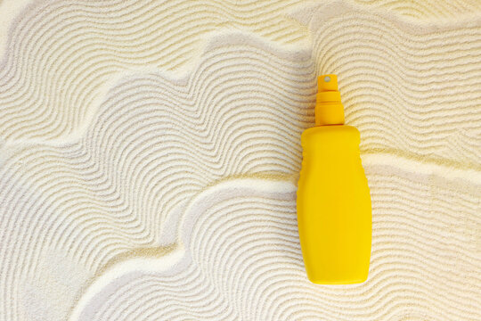 yellow cosmetic bottle with sunscreen cream spray on sand textured background. Cosmetic products  with spf. UV protection concept. Copy space