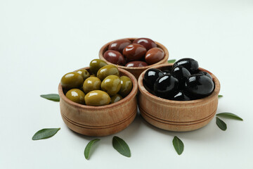 Wooden bowls of olives and leaves on white background
