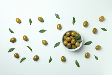 Bowl of green olives and leaves on white background, top view