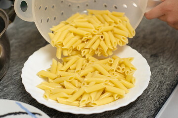 Serving drained macaroni on a white plate in the kitchen