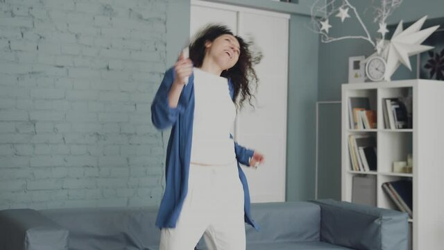 Excited happy curly haired woman dancing jumping, having fun, celebrating life