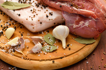 raw pork meat and lard with salt, spices and garlic on a cutting board, dark wooden background