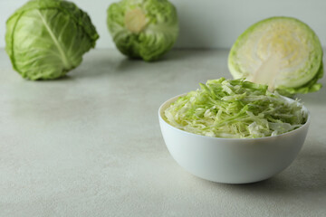 Bowl with sliced cabbage and fresh cabbage on white textured table