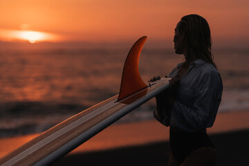 woman on tropical beach holding surfboard at sunset