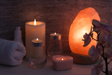 Himalayan salt lamp with orchid flower, oil, towel, candles in dark room. Spa, relax concept.