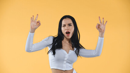 excited woman showing okay signs while winking at camera isolated on yellow