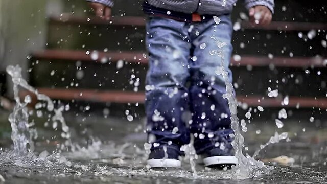 Child jumps into puddle in 240fps slow-motion. Kid having fun outside after rain