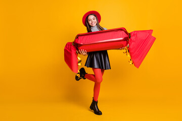 Full length photo of girlish pretty young girl wear black skirt red cap holding huge candy isolated yellow color background