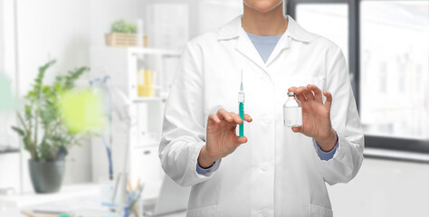 medicine, vaccination and healthcare concept - close up of female doctor or nurse with drug and syringe over medical office at hospital background