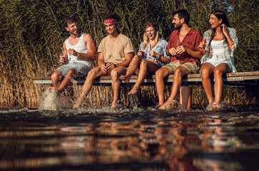 Group of friends sitting on the edge of a pier having fun and enjoying a summer day at the lake.