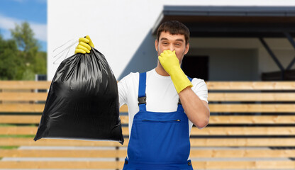 profession, cleaning service and people concept - male worker or cleaner in overall and gloves with stinky garbage bag over living house background