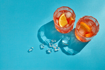 Cocktail. Two glasses with cool beverages, sliced oranges and ice on blue background with shadow. Top view with copy space