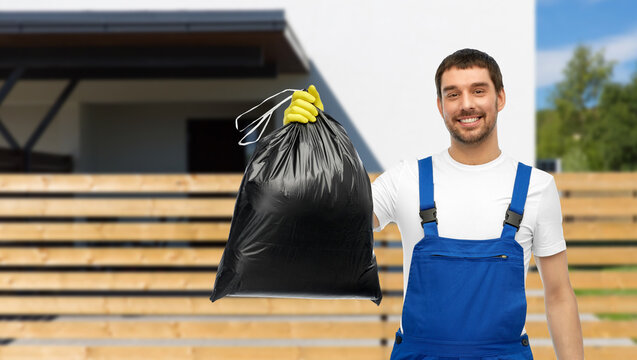 Profession, Cleaning Service And People Concept - Happy Smiling Male Worker Or Cleaner In Overall And Gloves Showing Garbage Bag Over Living House Background