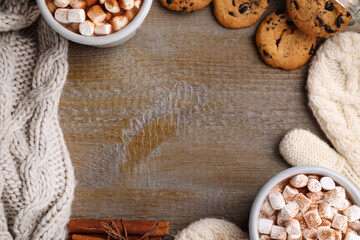 Frame made with cocoa drink, cookies and warm clothes on wooden table, flat lay. Space for text