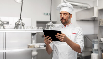 cooking, culinary and people concept - male chef in toque with tablet pc computer over restaurant kitchen background