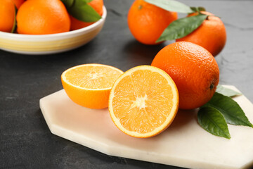 Whole and cut delicious ripe oranges on black table