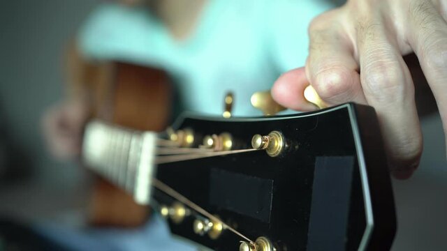 Tuning acoustic guitar string by adjusting tuning machines