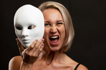 Screaming young blonde woman with a white mime mask in her hand. Change of emotions. Black...