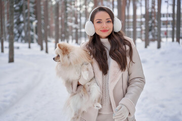 Young pretty beautiful girl in white pullover, skirt, boots, coat and fur headphones walking in...