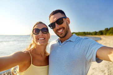 Obraz premium leisure, relationships and people concept - happy couple in sunglasses hugging and taking selfie on summer beach