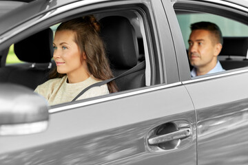 transportation, vehicle and people concept - happy smiling female driver driving car with male passenger