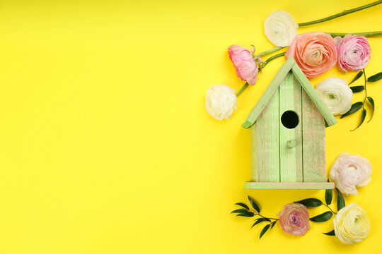 Stylish bird house and fresh eustomas on yellow background, flat lay. Space for text