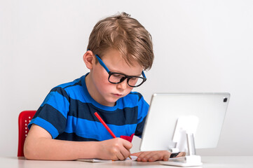 Naklejka na ściany i meble Pupil boy on distance lesson. Having video conference call using webcam. Online education at home during quarantine. Learning and working from home. Kid in glasses is drawing