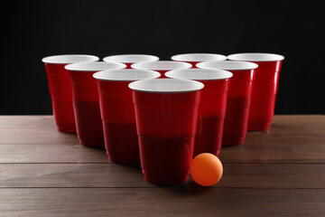 Plastic cups and ball for beer pong on wooden table against black background